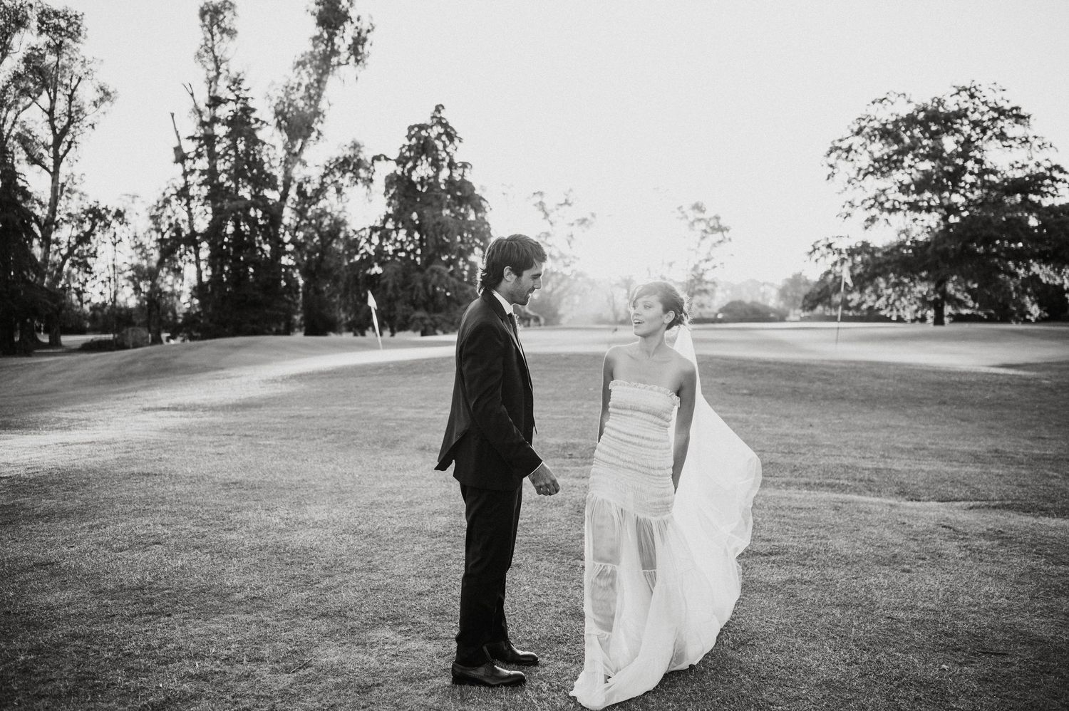 Wedding couple walking across a scenic grassy field.