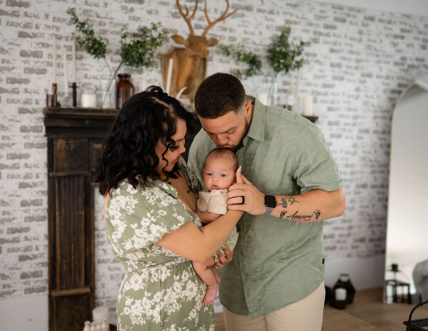A couple shares tender moments while holding their newborn baby wrapped in a pink blanket on a couch.