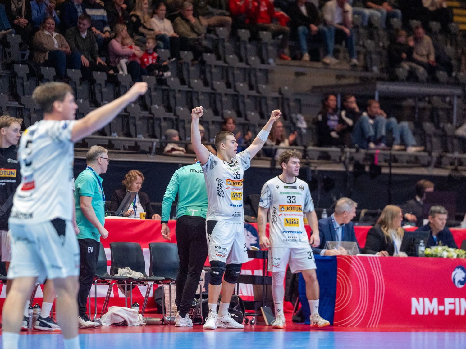 Spillere på benken jubler med armene i været under en håndballkamp i idrettshall.