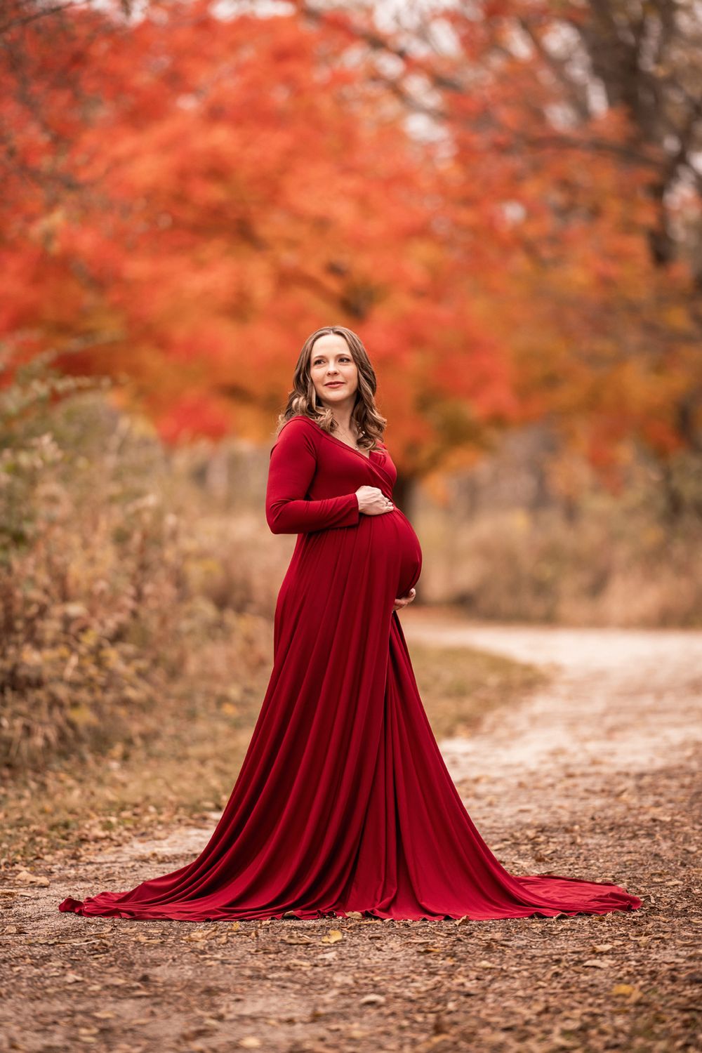 Fall maternity portrait of woman in long red dress.
