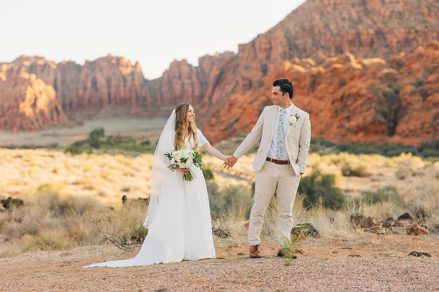 Newlywed couple poses in front of stunning red rock formations at Snow Canyon State Park during golden hour.