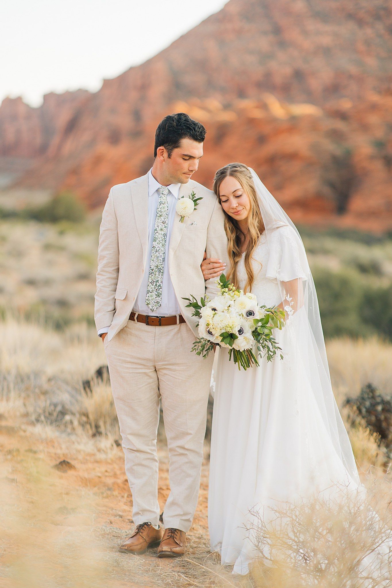 A romantic desert wedding photo session with red rock formations and desert brush in the background.