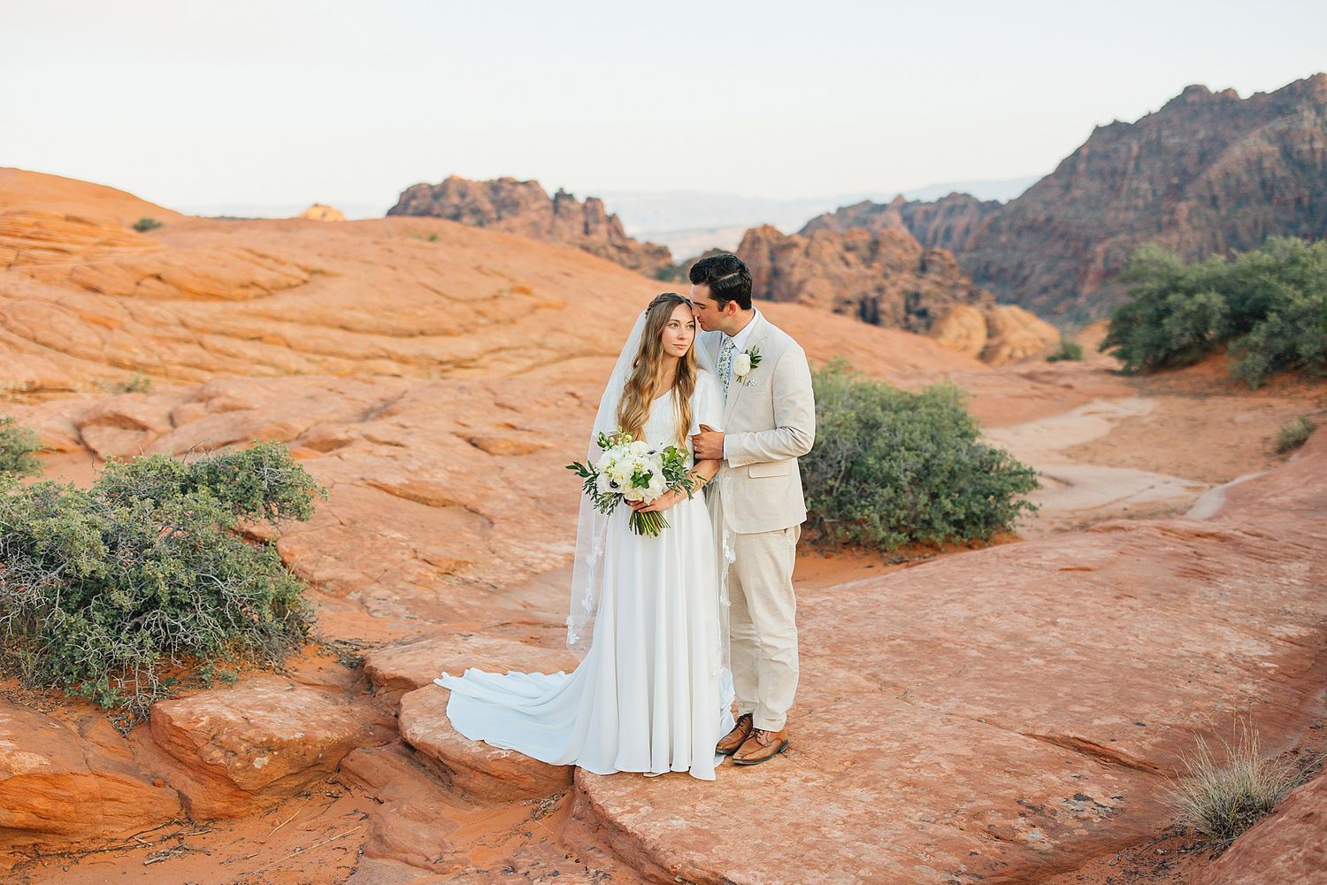 Couple walking along scenic red rock formations in Snow Canyon State Park during golden hour sunset.