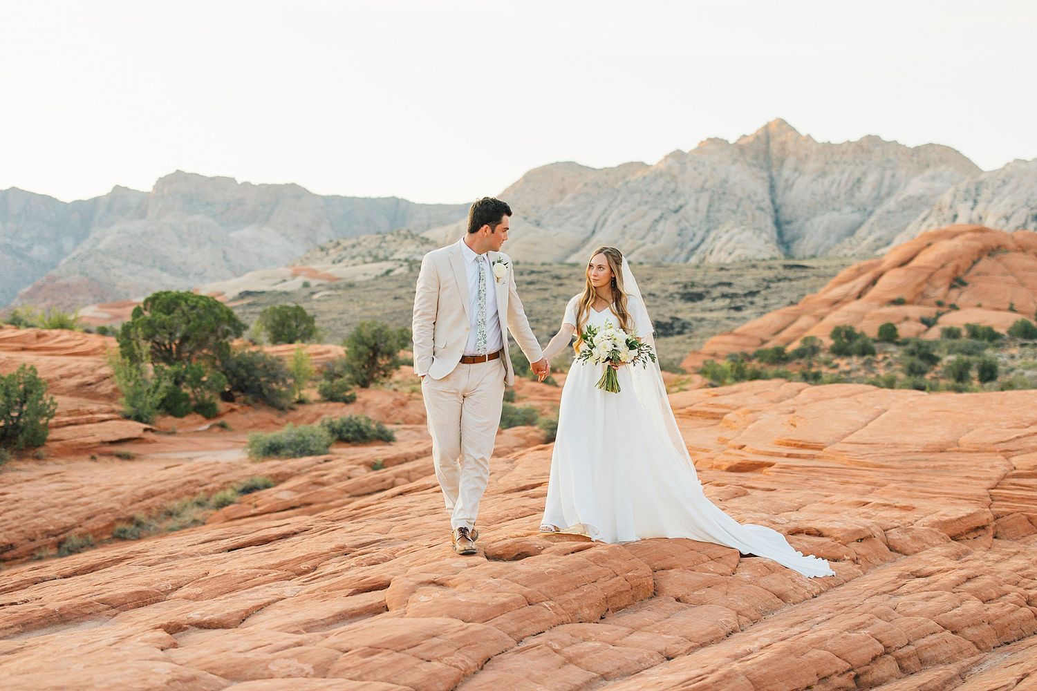 Wedding photography session on vibrant orange sandstone cliffs with mountain backdrop at sunset.
