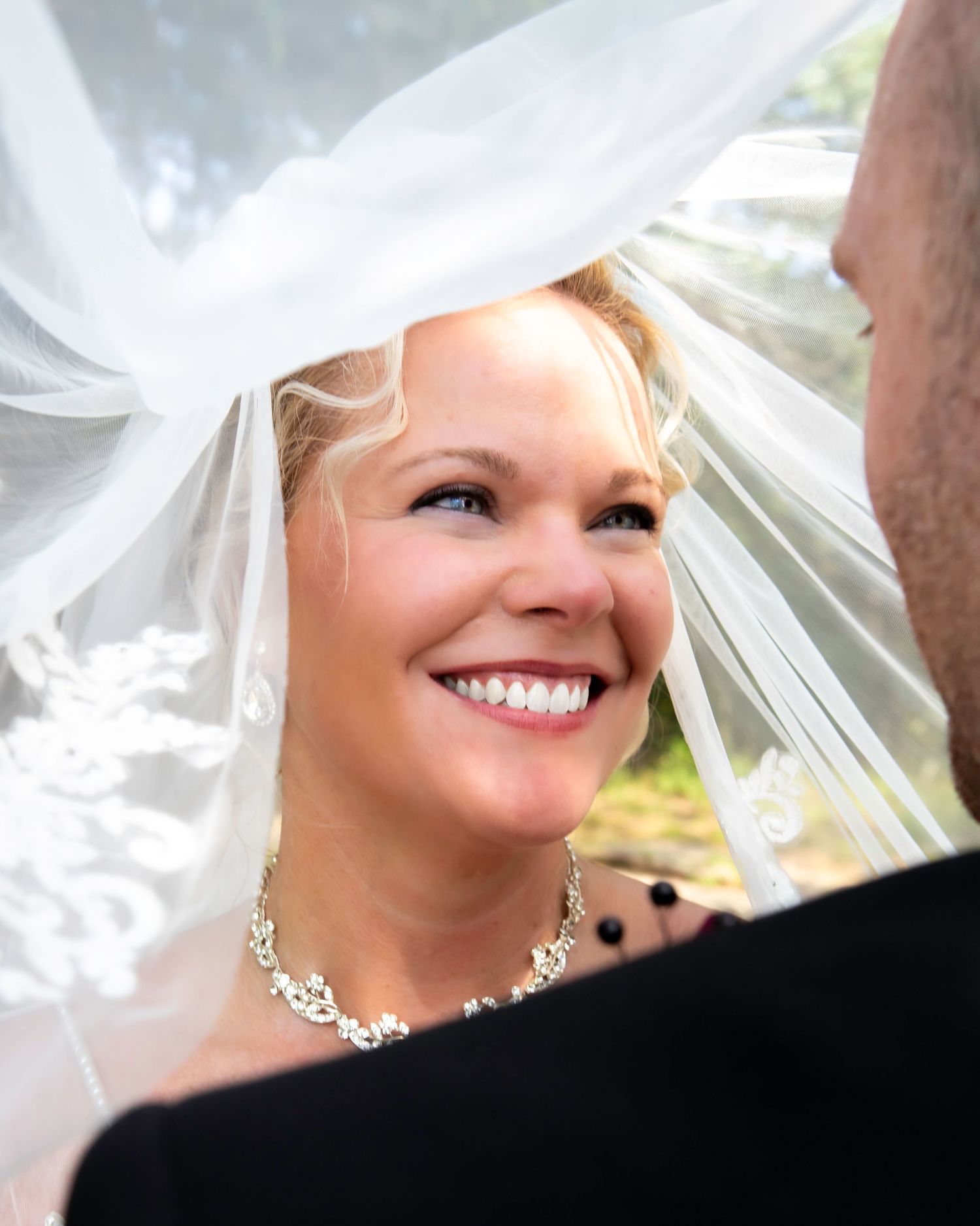 Close-up view of a bride wearing a white veil and sparkling jewelry in natural lighting.