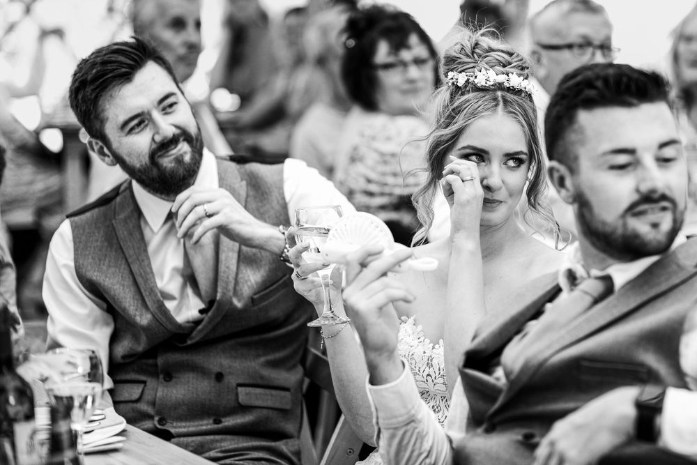 Emotional bride wiping tears while groom holds her hand during heartfelt wedding speeches.