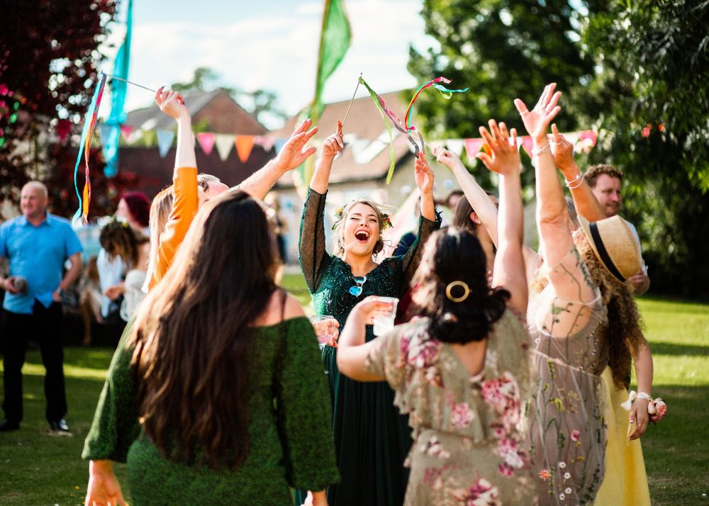Wedding guests dance joyfully with arms raised at a colorful outdoor garden celebration.