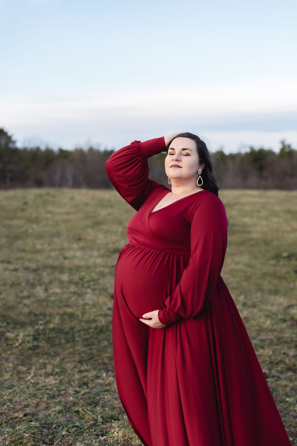 A dramatic pose of a pregnant women wearing a red maternity gown at Pitcher Mountain Farm in Stoddard, New Hampshire for winter shoot.