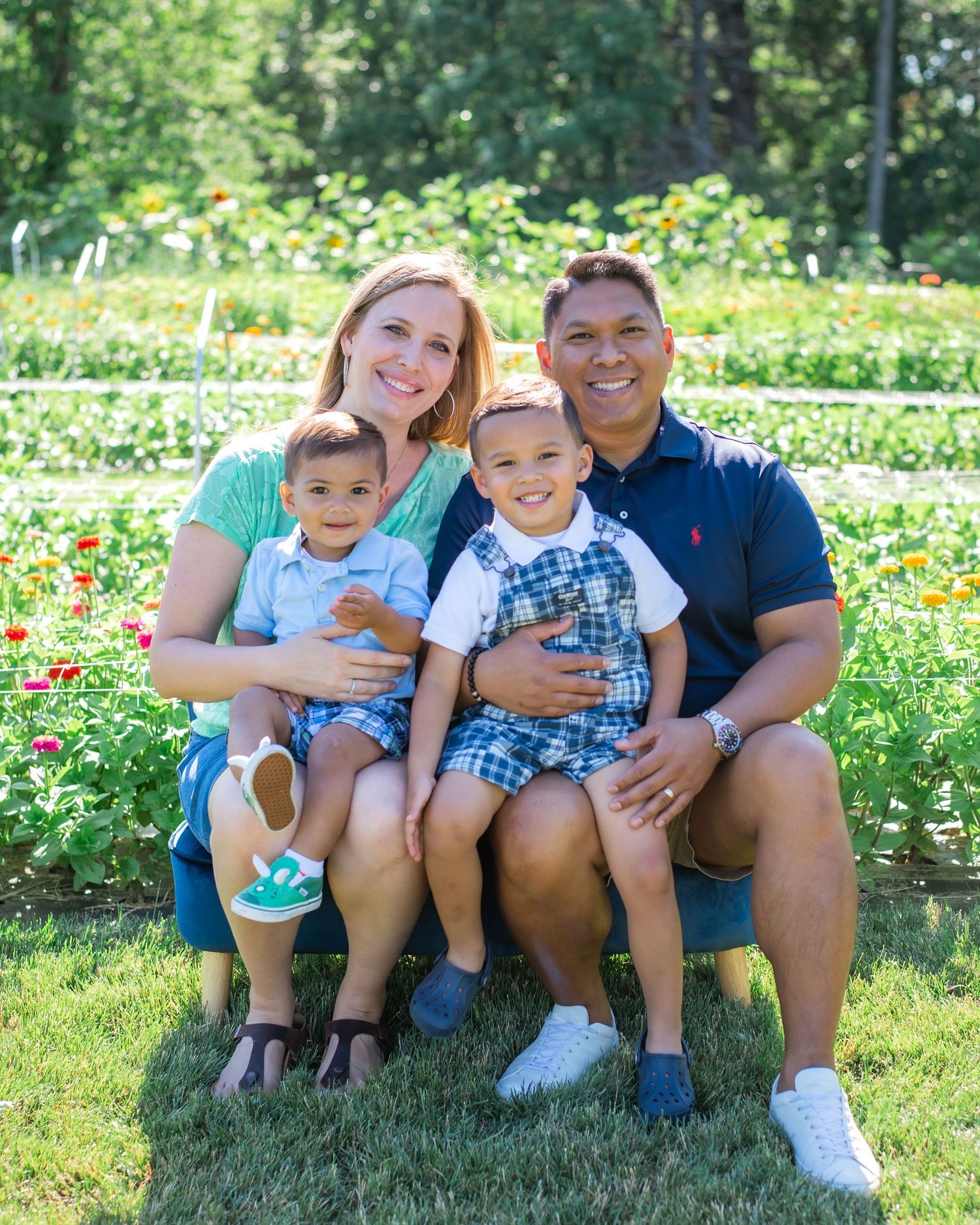 A family sits together outdoors on green grass surrounded by wildflowers on a sunny summer day.