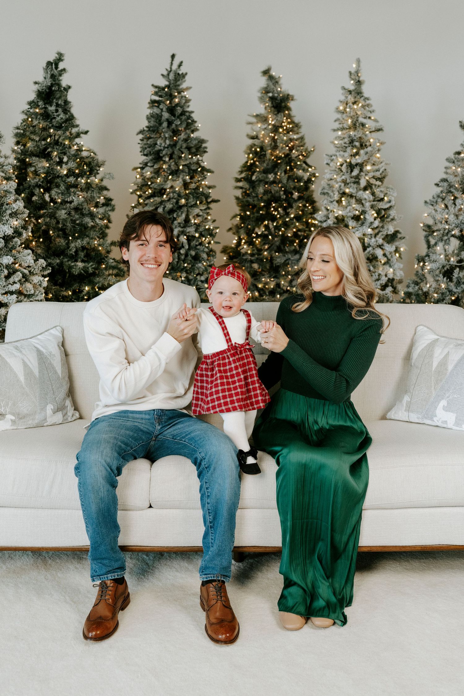 Family poses on white couch in front of lit Christmas trees during holiday photo session.