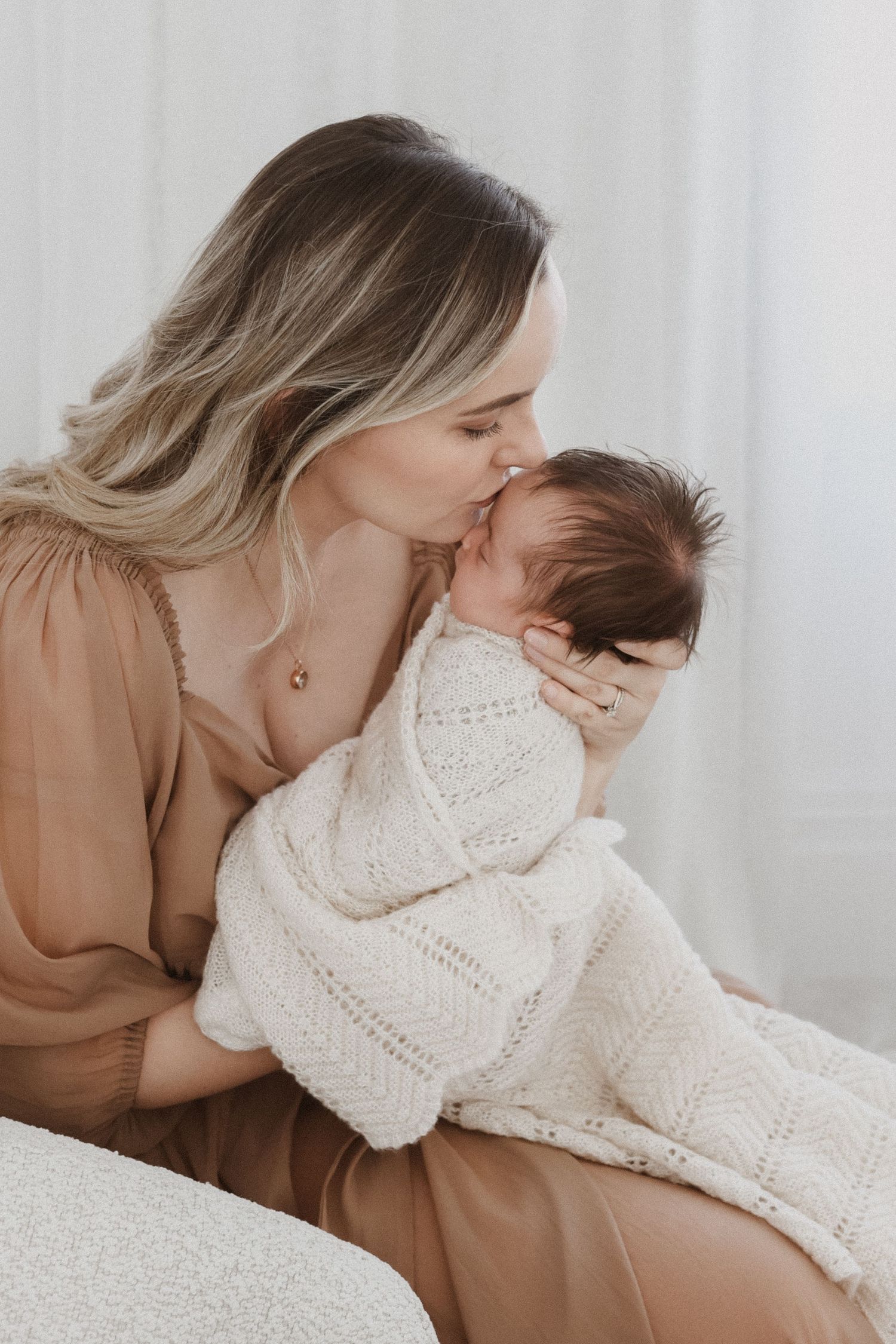 A tender series of moments showing a parent in white embracing a baby wearing a cream knit sweater against a light background.