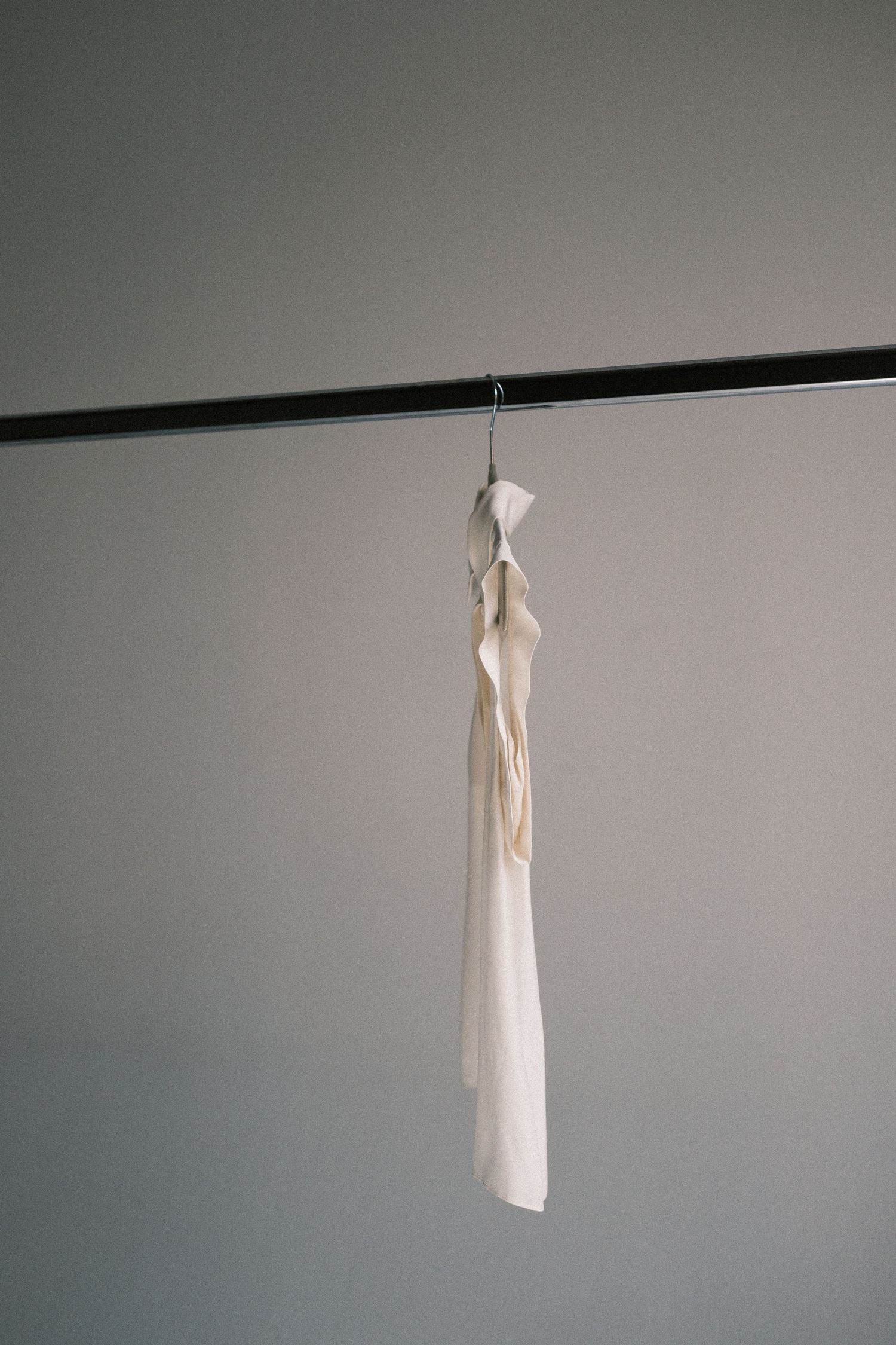 A white dress suspended in mid-air against a gray wall, shown in a sequence of four minimalist photographs.