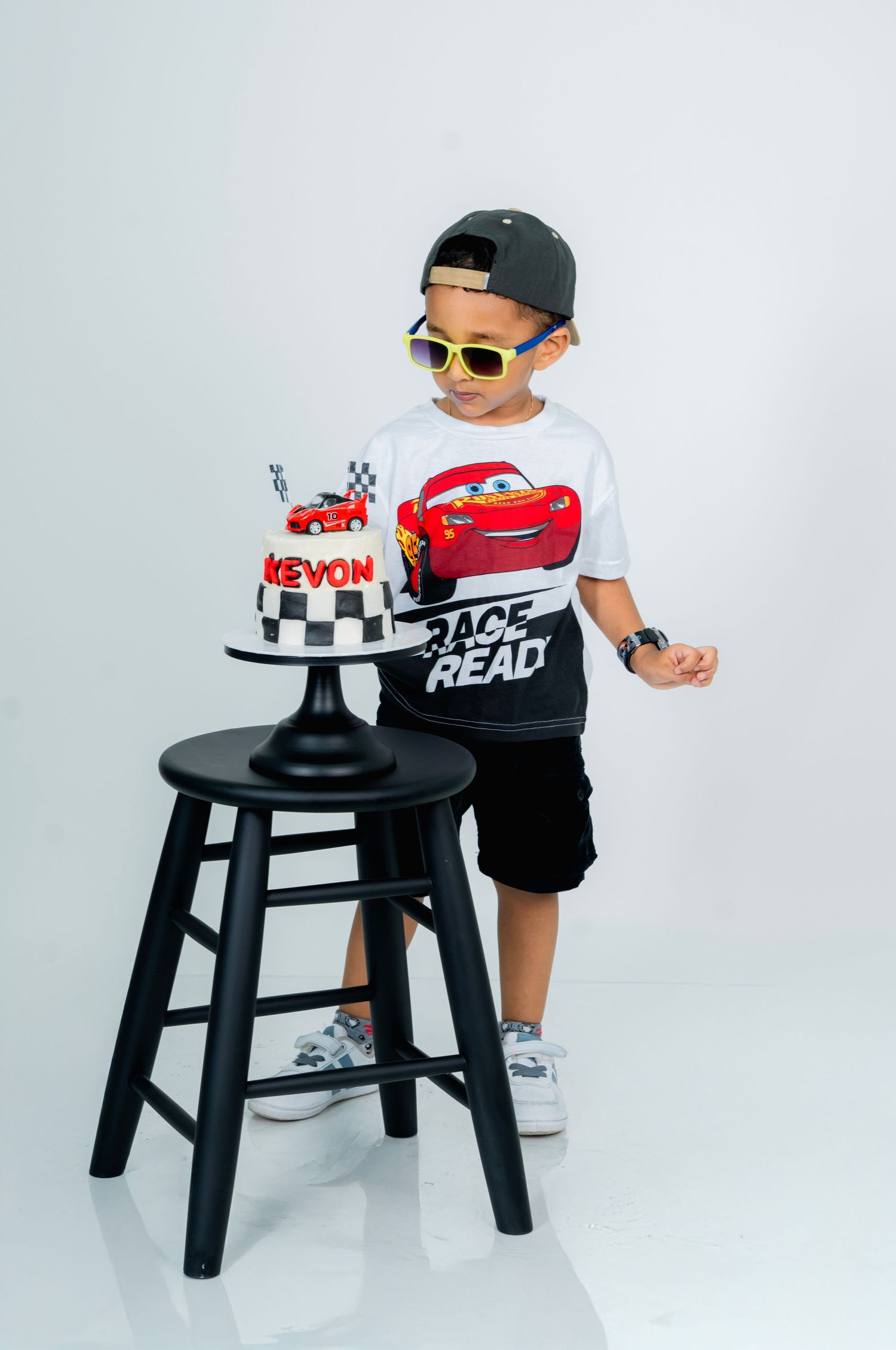 Three sequential photos show a child playing with a black stool and toy cars against a white studio backdrop.