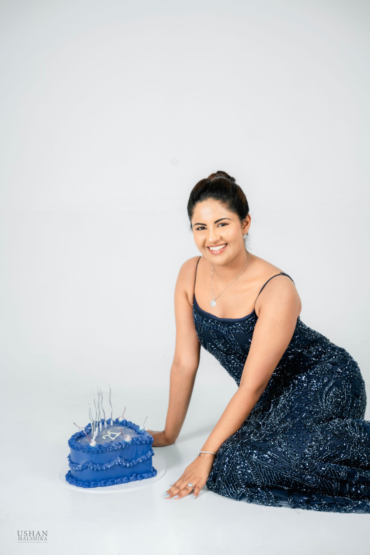 A person in a sparkling navy blue evening gown poses gracefully on a white backdrop with a blue decorative element.