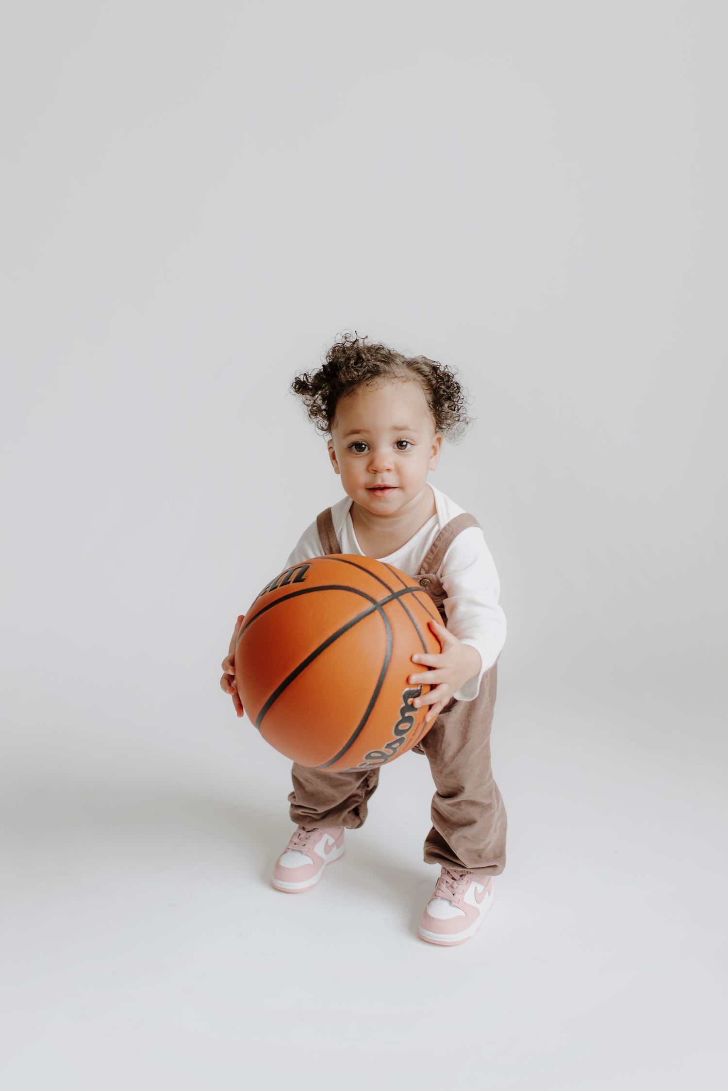 Toddler playing with basketball against white background in studio photography session.
