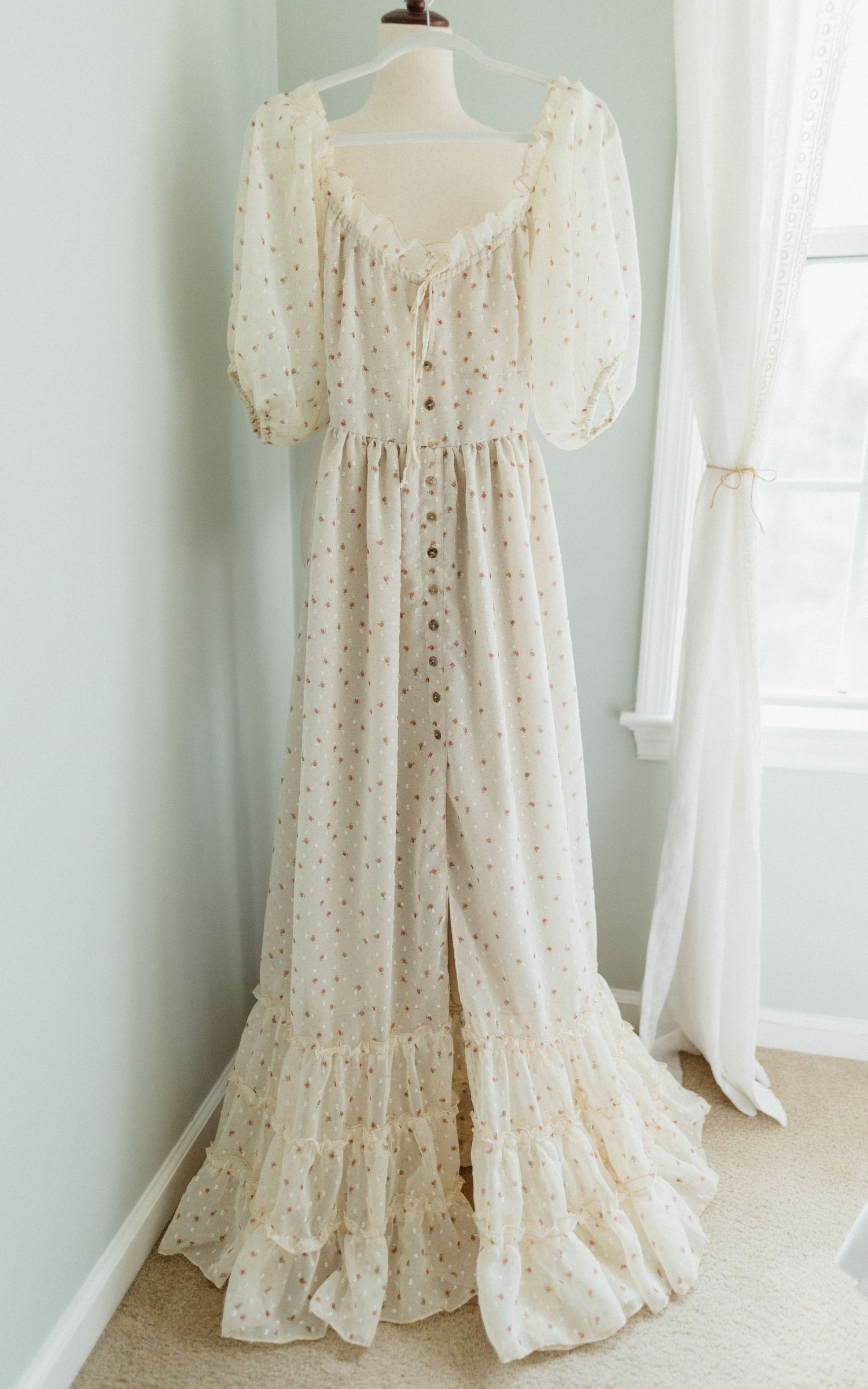 Vintage cream-colored maxi dress with puff sleeves and gathered neckline displayed on white mannequin against pale wall.