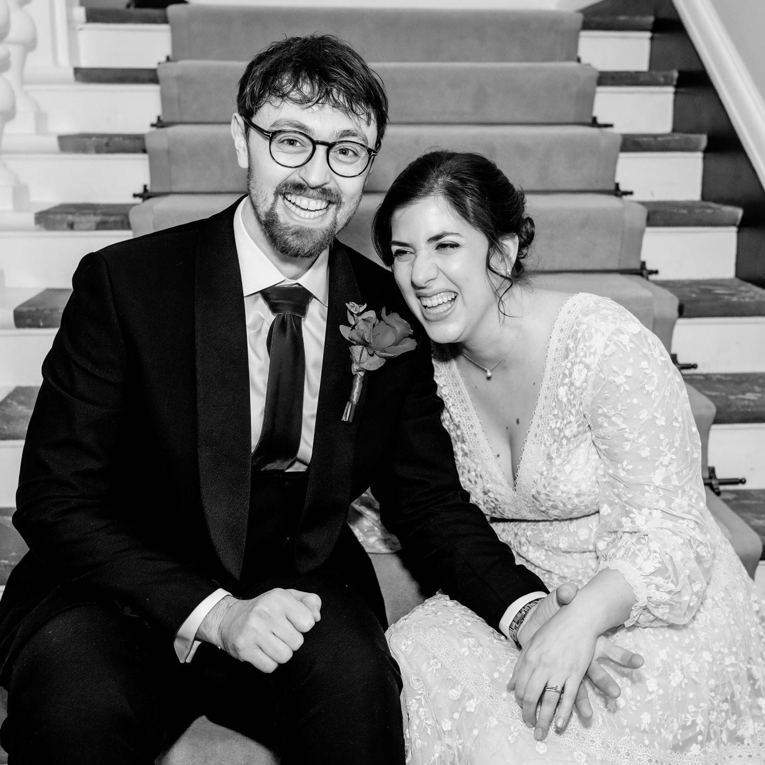 Black and white wedding photo showing a couple sitting on stairs, smiling and laughing together.