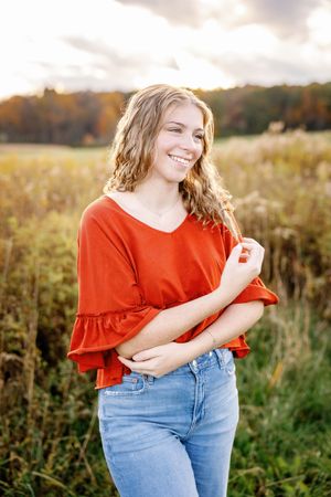 Candid outdoor portraits in orange top and jeans against golden sunset field.