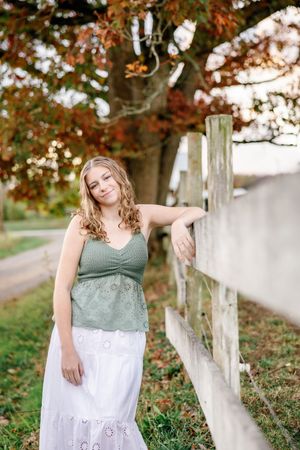 Rustic outdoor portraits by white fence wearing sage green and white dress.