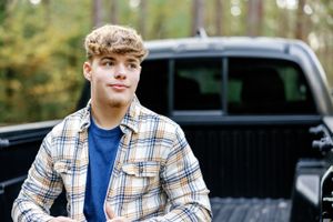 Senior wearing plaid shirt and blue top in outdoor setting.