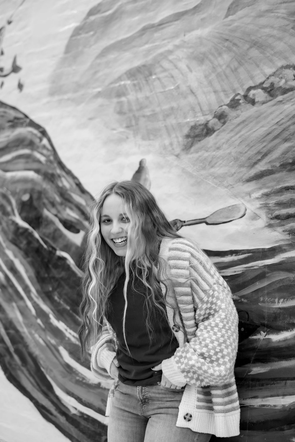Black and white portrait against textured rock wall with person in striped cardigan.