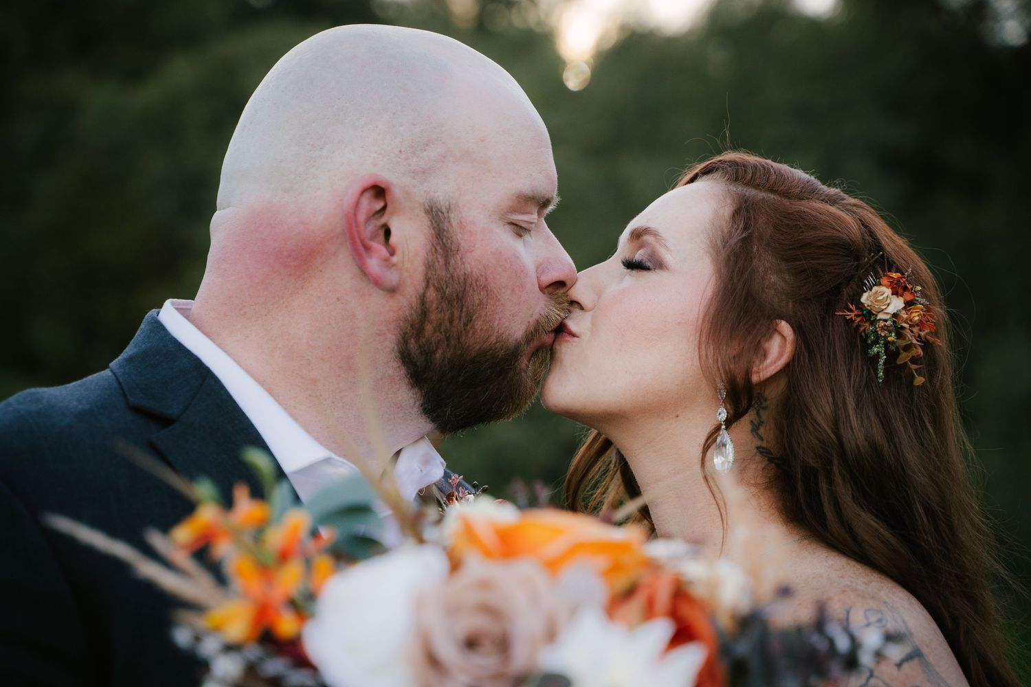 Romantic sunset wedding couple shares intimate kiss surrounded by orange lilies and greenery in garden setting.