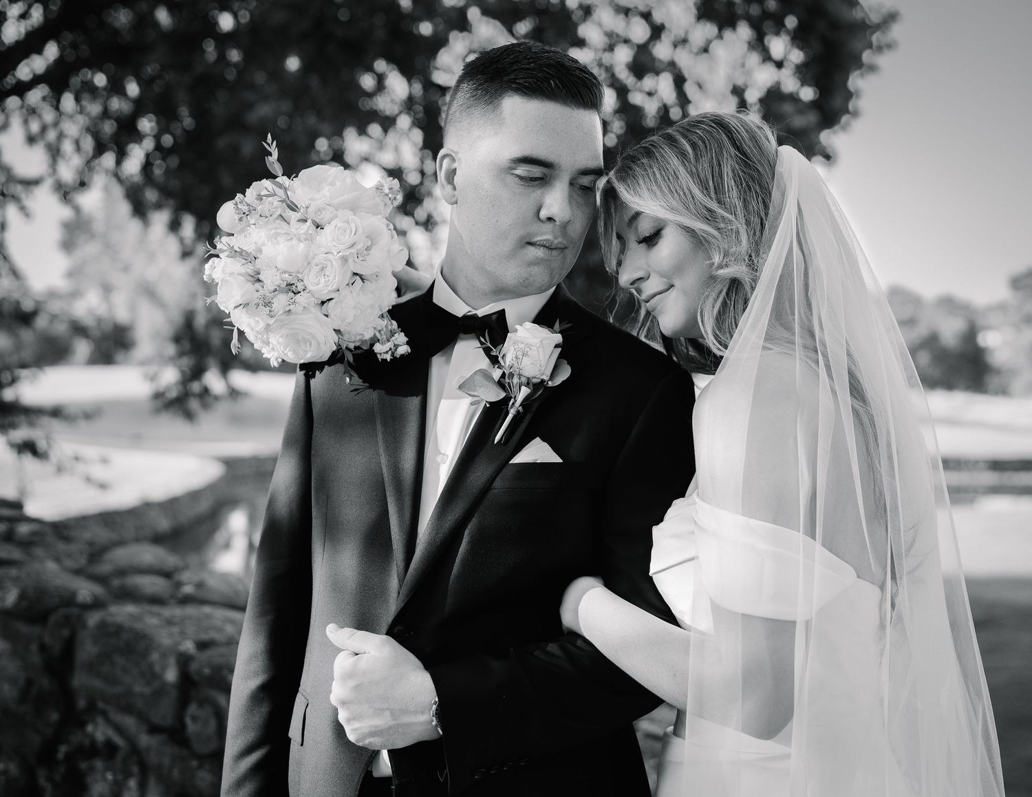 Romantic sunset wedding couple shares intimate kiss surrounded by orange lilies and greenery in garden setting.