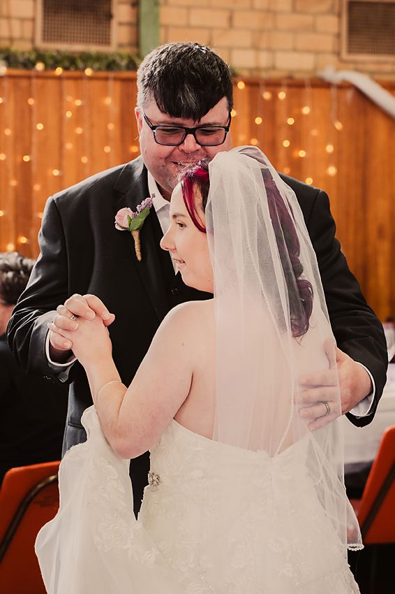 A bride and groom share a joyful moment while cutting their wedding cake decorated with pink roses.