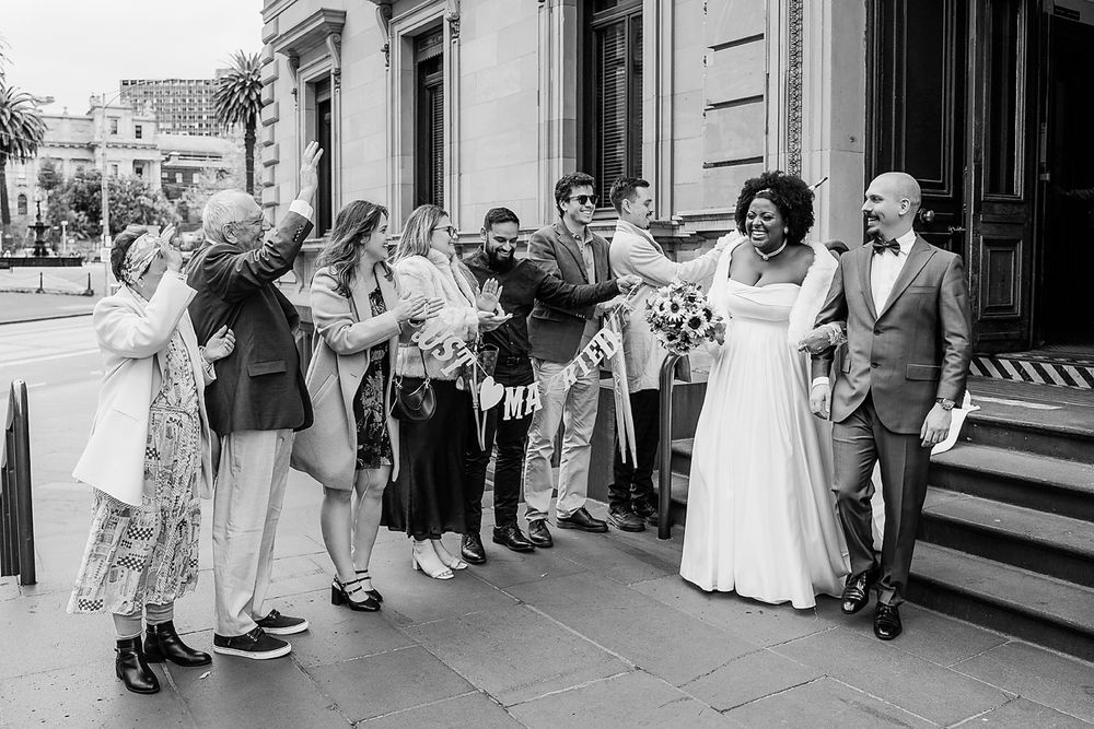 Black and white photo showing a line of guests in formal attire standing outside a storefront.