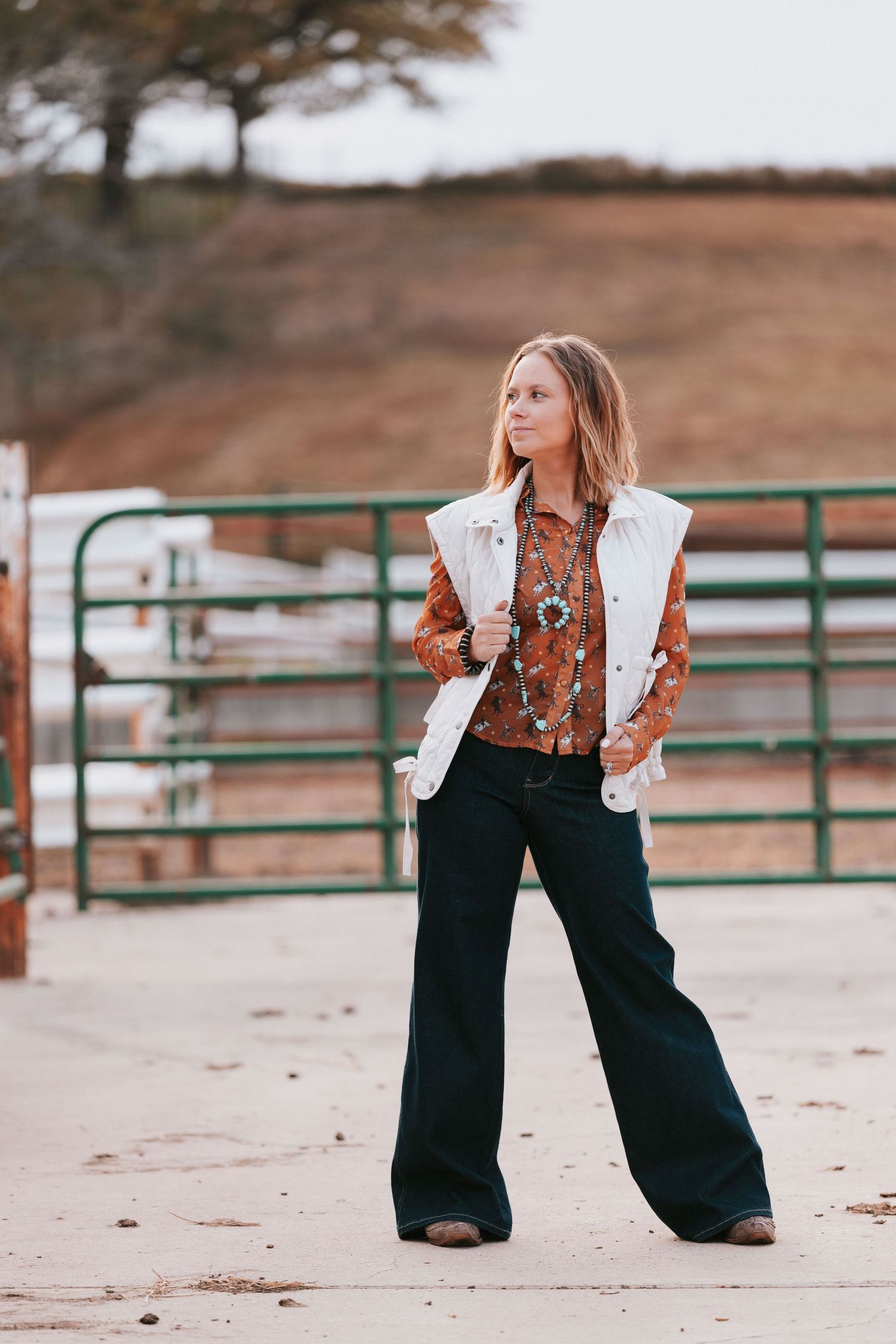 Person in vintage-inspired outfit with ruffled blouse and dark wide-leg pants poses in outdoor setting.