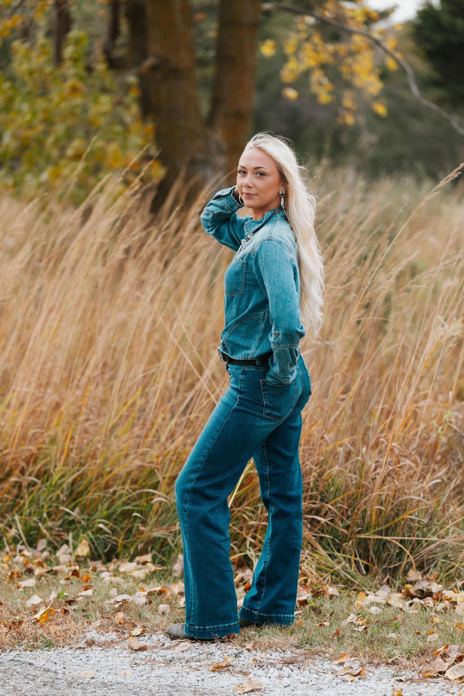 A person wearing denim overalls and a teal sweater plays joyfully in a field of tall autumn grass.
