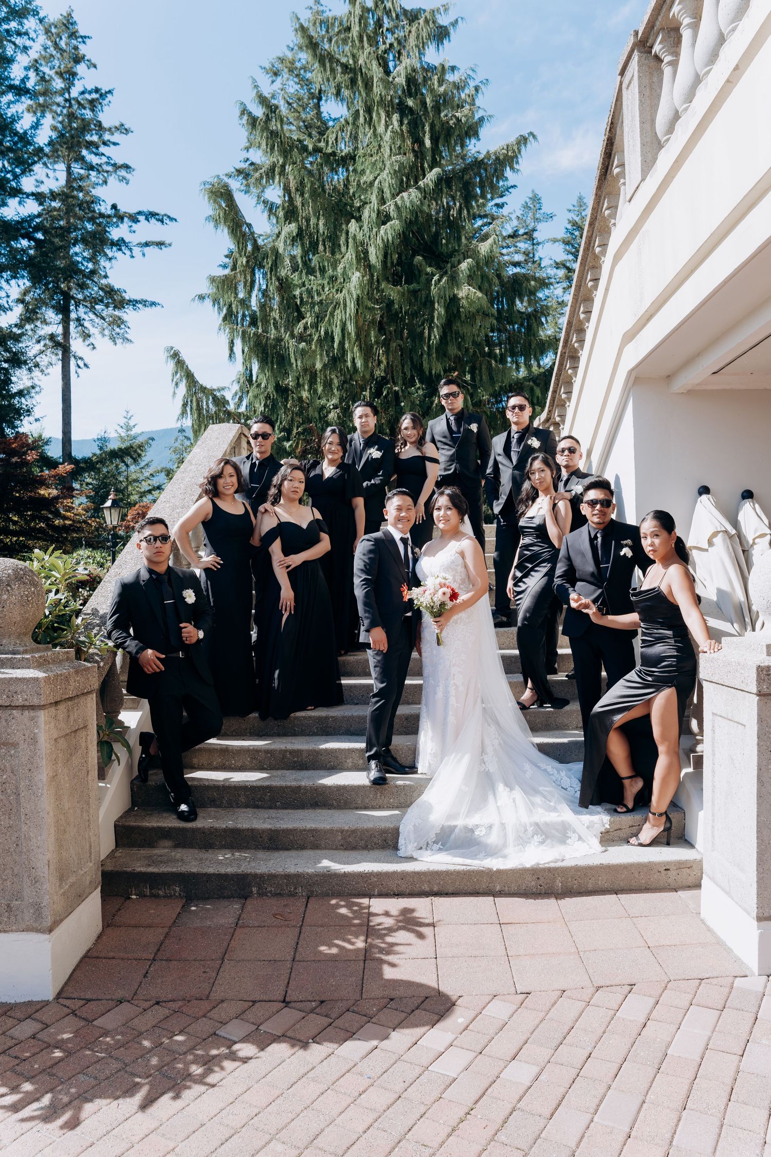 Wedding party in black and white attire poses on outdoor stone steps in a candid progression of group photos.