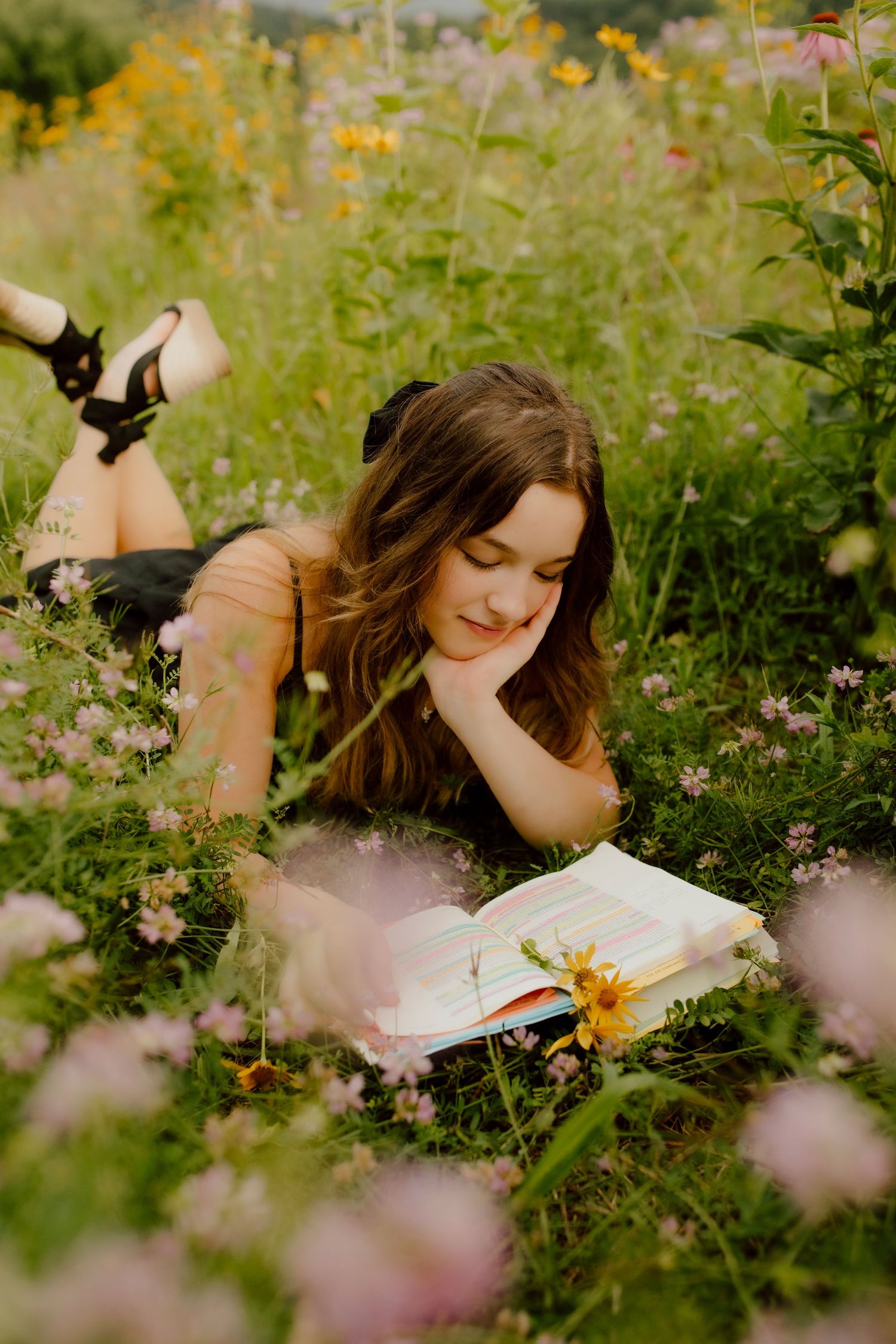 Young woman lying in a wildflower meadow reading a book on a sunny day.