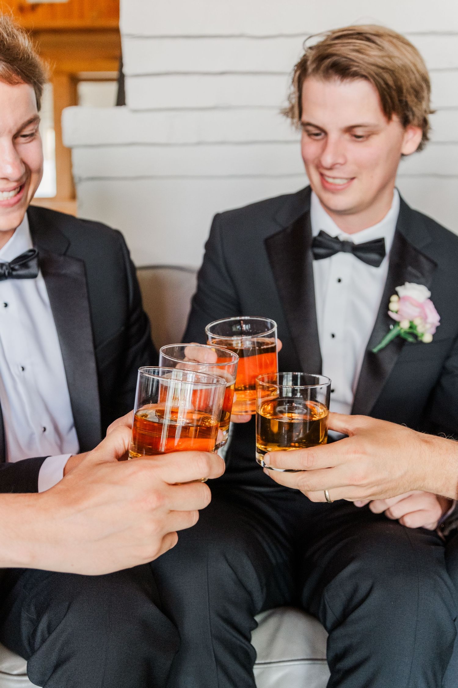 Wedding party in formal attire toasts with whiskey glasses during celebration.