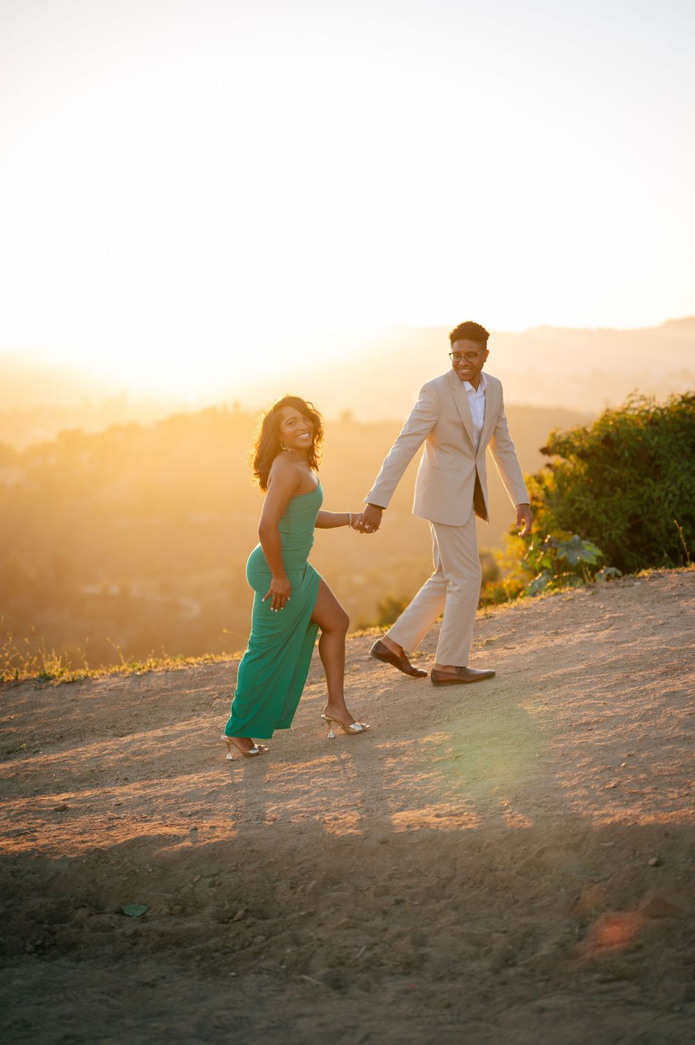 A couple walks hand in hand on a sandy hill during golden hour sunset creating romantic silhouettes.