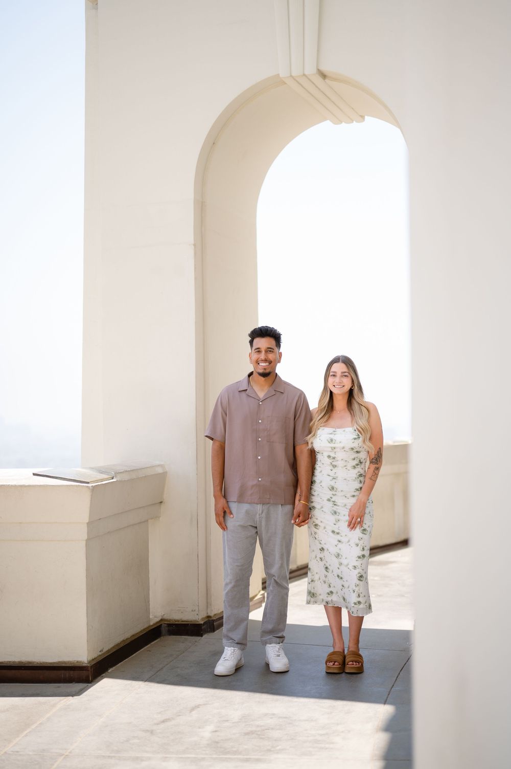 A couple poses together in a minimalist white archway corridor with natural lighting.