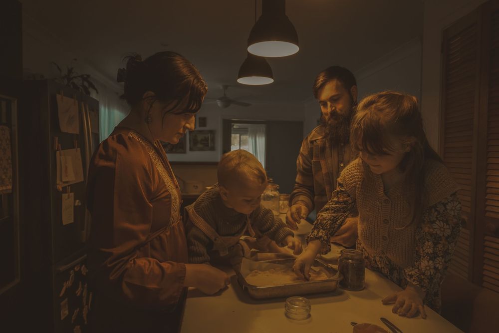 A group of people gather around a table in a dimly lit room with warm lighting, working on a project together.