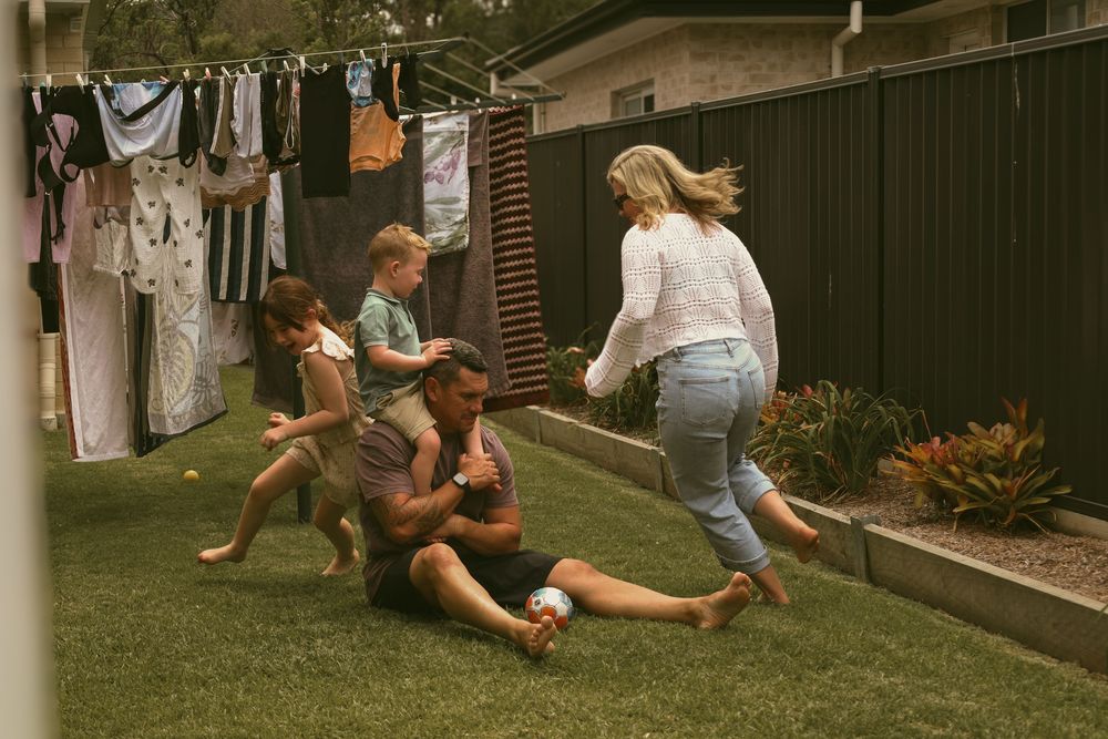 A group plays together on a backyard lawn near a clothesline on a sunny afternoon.