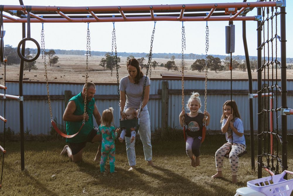 Children play on outdoor playground equipment at a park with swings and climbing structures.