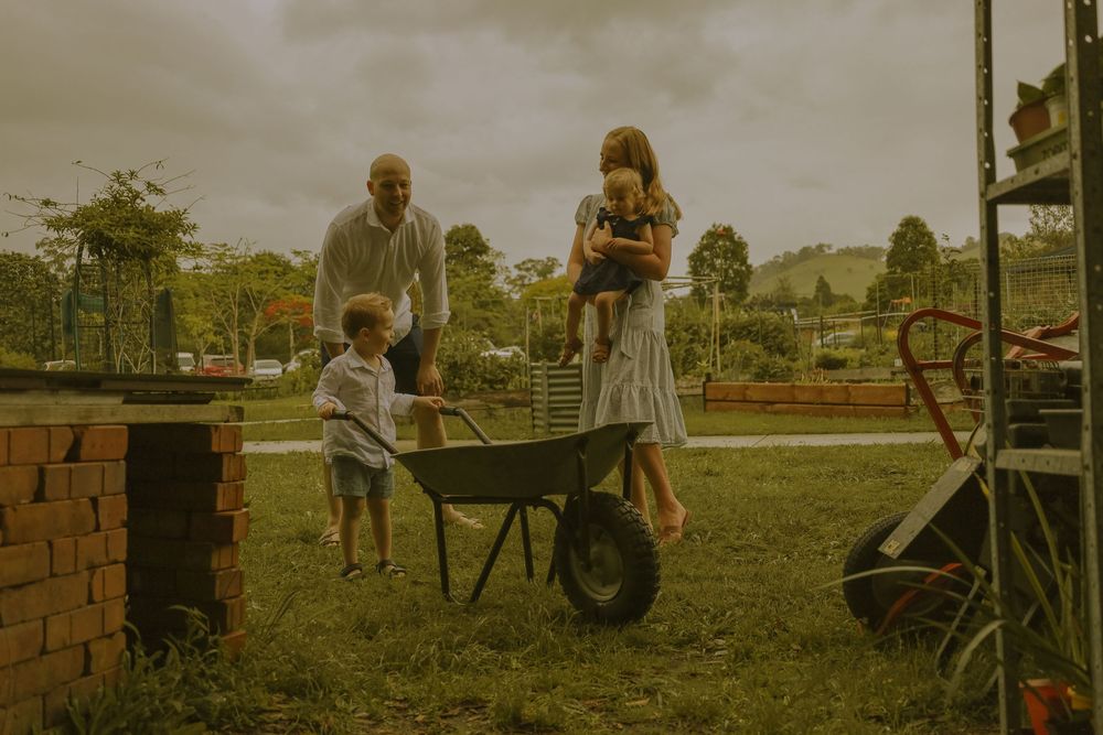 People sit and relax on outdoor chairs and benches in a grassy park area on a sunny afternoon.