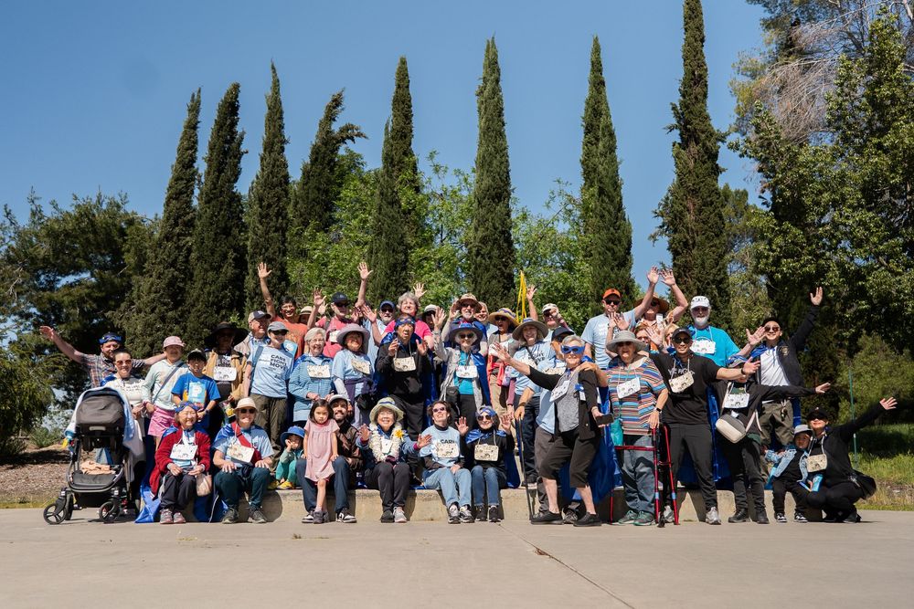 Large group of people seated outdoors with cypress trees in the background.
