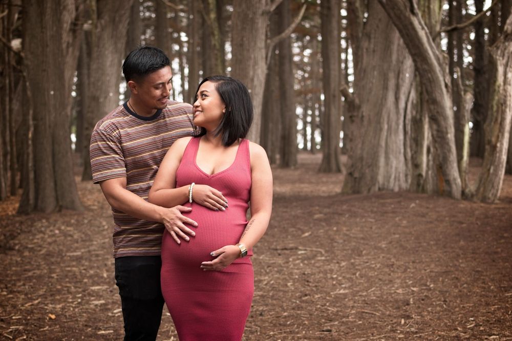 Couple sharing an intimate moment on a tree-lined path in a forest setting.