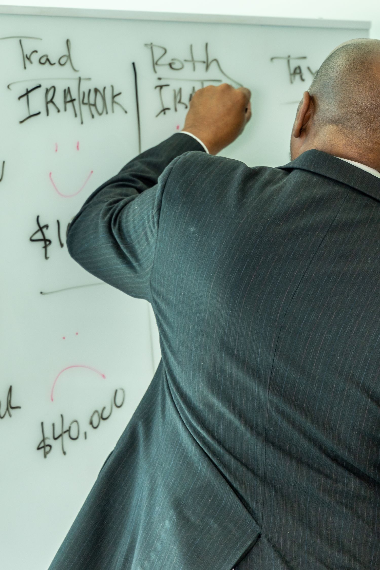 Person in a dark suit writes on a white board during a business presentation or meeting.