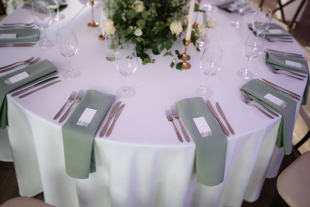 Round banquet table with crisp white linens and sage green napkins set for formal dining.