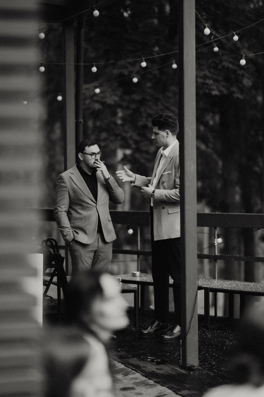 Two guests having a conversation on an outdoor patio with string lights overhead.