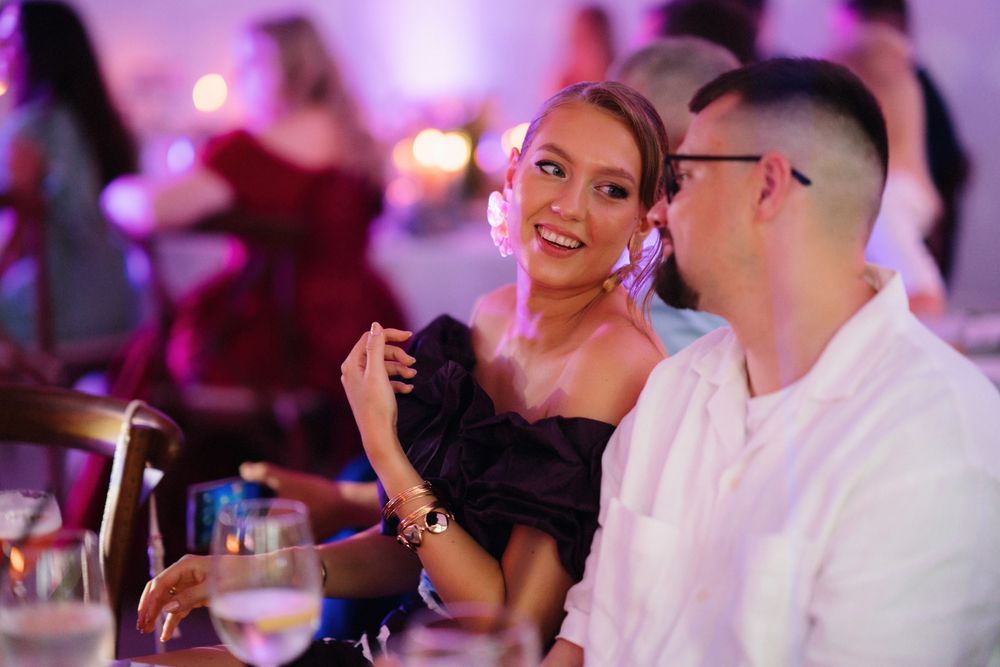 Couple enjoying drinks and conversation at a reception with purple mood lighting.
