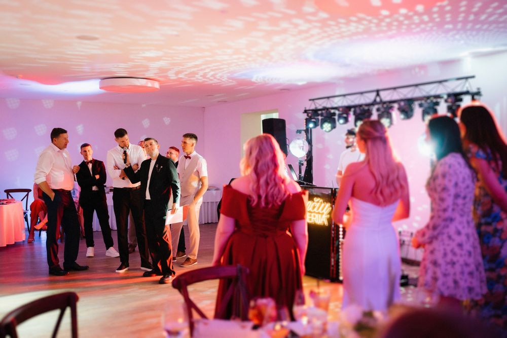 Wedding reception dance floor illuminated with pink lighting as guests celebrate and dance together.
