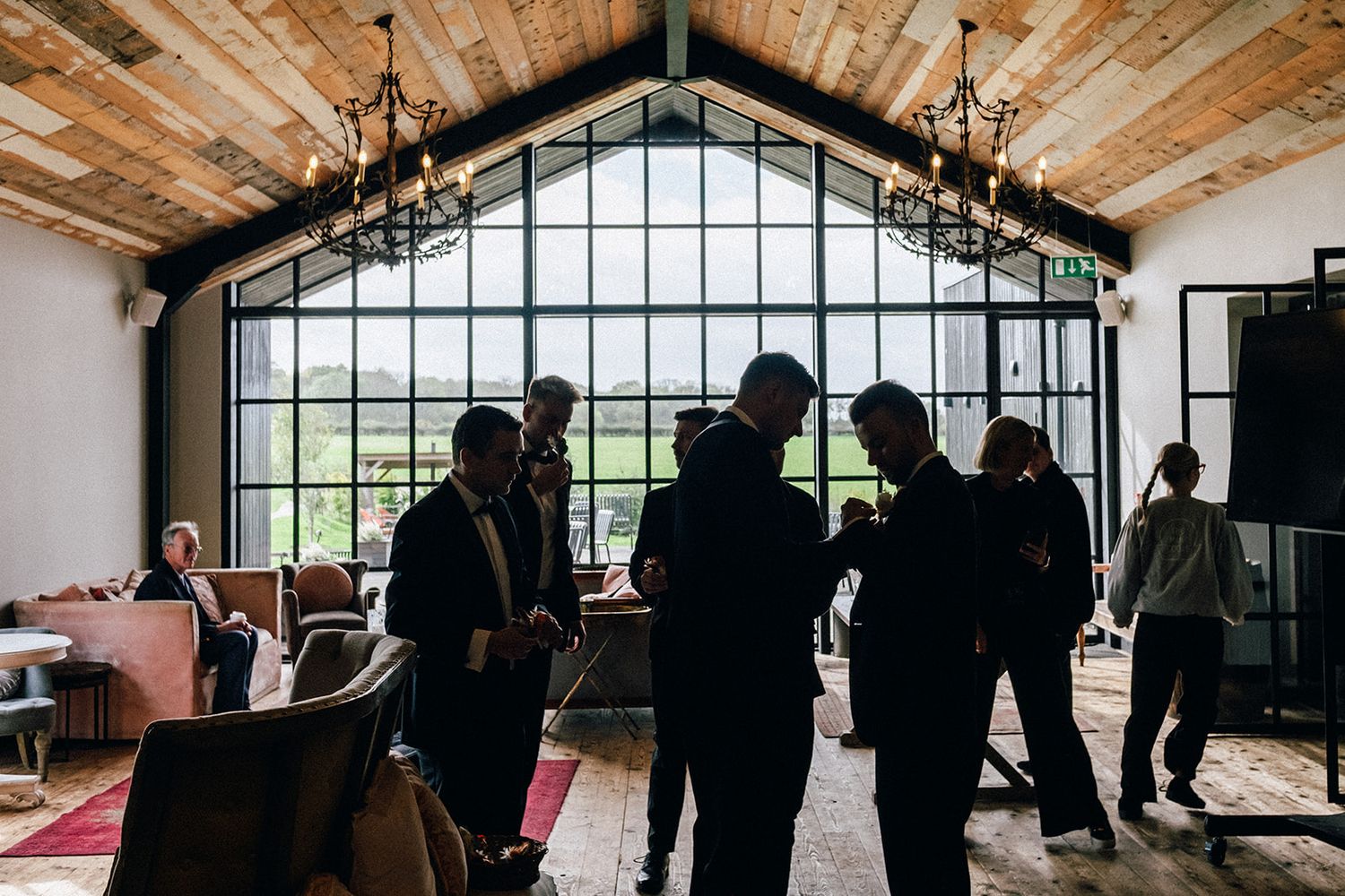 The Baby Barn - Silhouettes of people gathered in a rustic venue with wooden ceiling and large arched window overlooking scenic landscape.