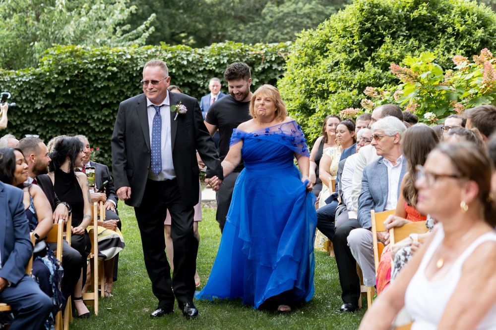 Wedding guests mingle and socialize in an outdoor garden setting during a sunny afternoon reception.