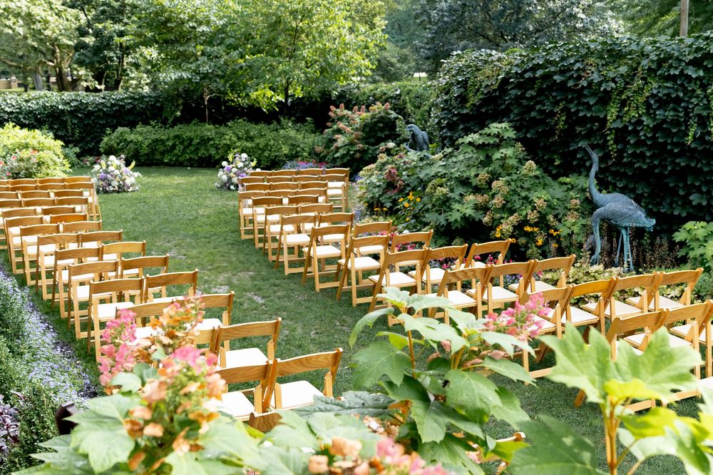 Wooden chairs arranged in rows for an outdoor garden wedding ceremony with lush greenery and flowers.